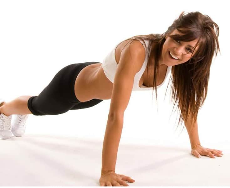 donna sorridente mentre fa una variazione di plank per tonificare gli addominali.