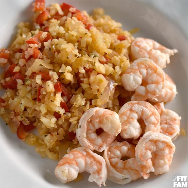 a plate of shrimp with some cauliflower rice on the side, seasoning is cajun